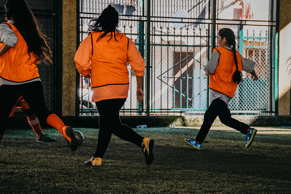 Afghan Refugee girls playing football in orange hi-vis vests