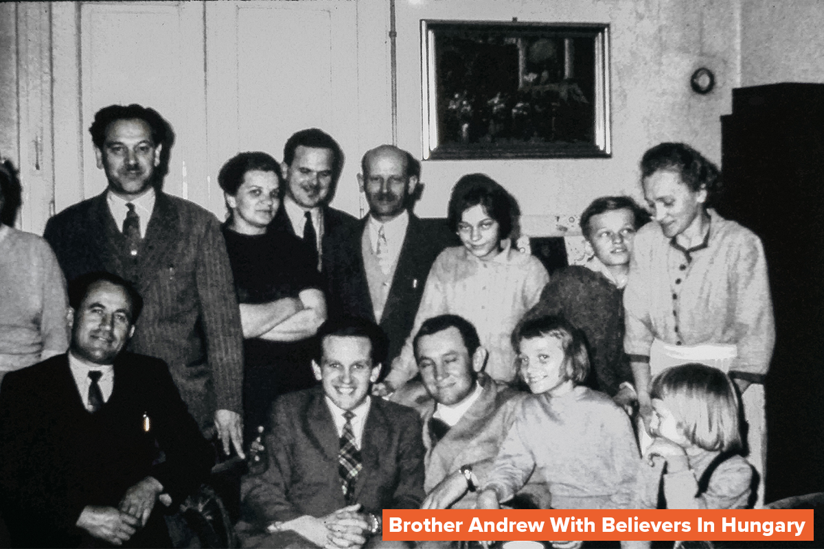 a black and white photo of Open Doors founder Brother Andrew sitting among a group of Christian believers in Hungary