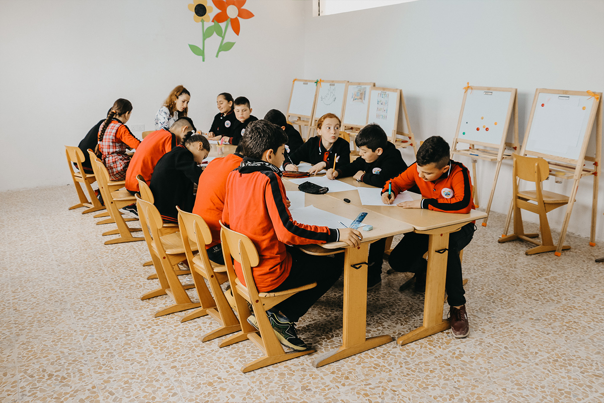 13 students sitting around a table with their teacher drawing and colouring
